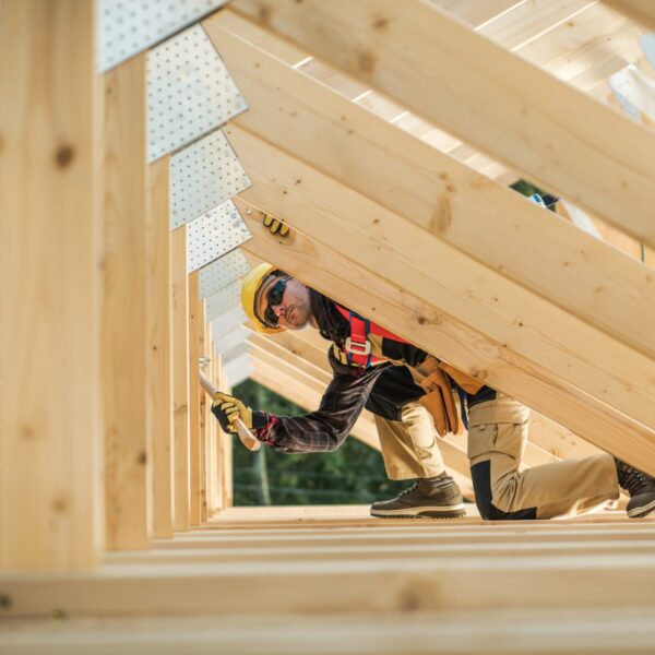 Caucasian Contractor Working with Wooden House Frame in the Attic Section.
